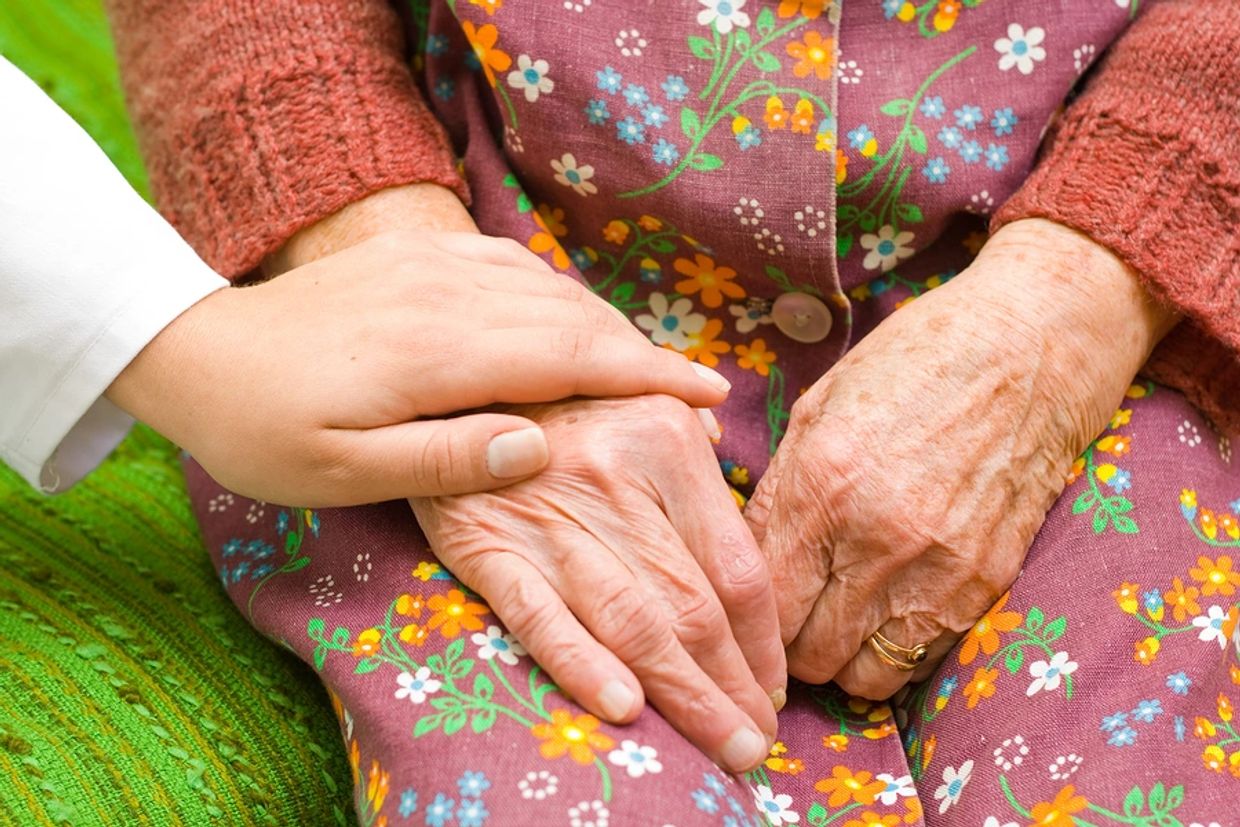 A young hand comforting an elderly hand on a floral dress.