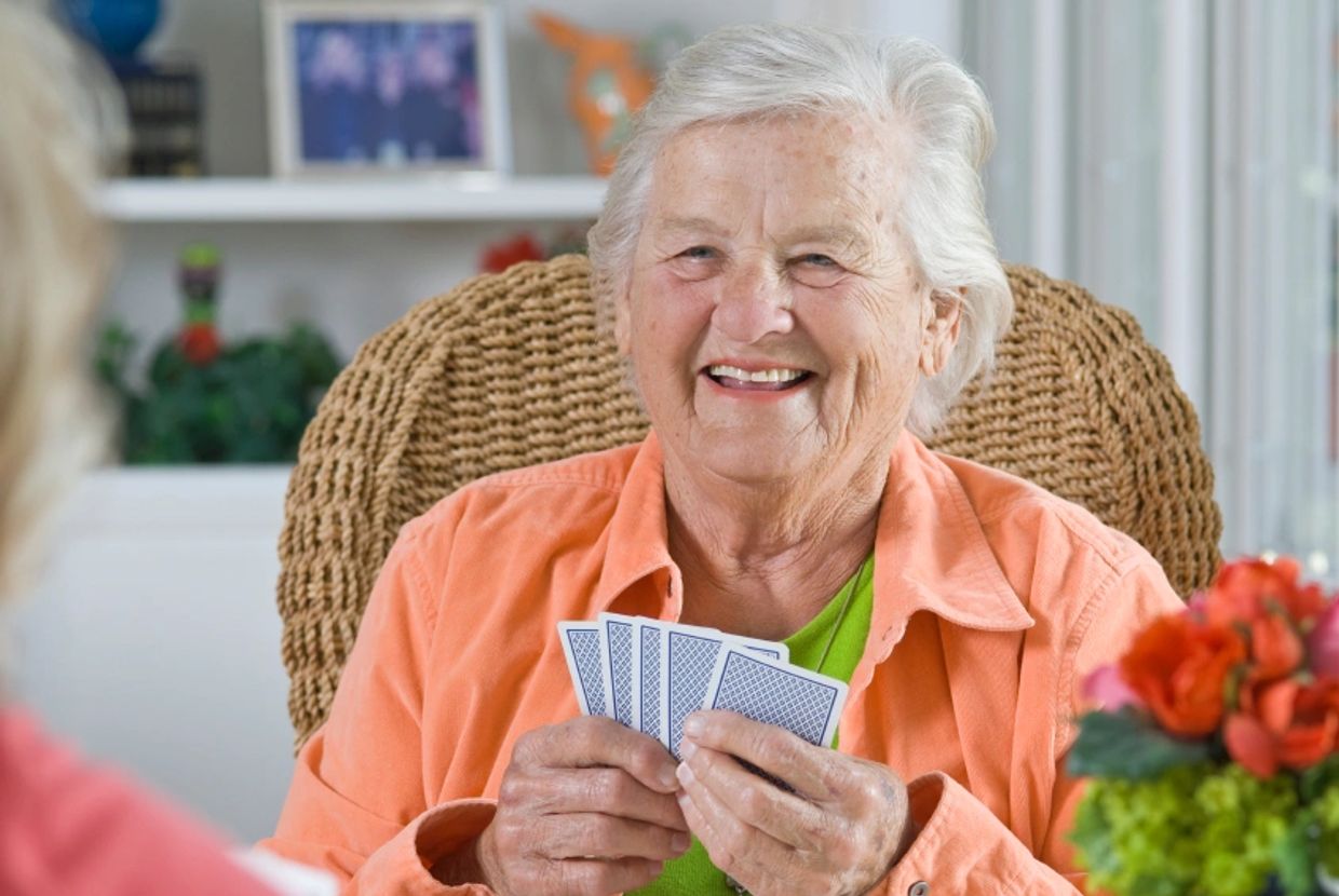 Elderly woman smiling while holding playing cards indoors.