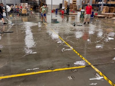 Workers cleaning a wet warehouse floor with mops.