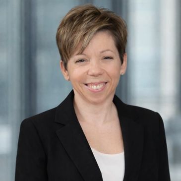 Professional woman smiling in business attire with a blurred office background.