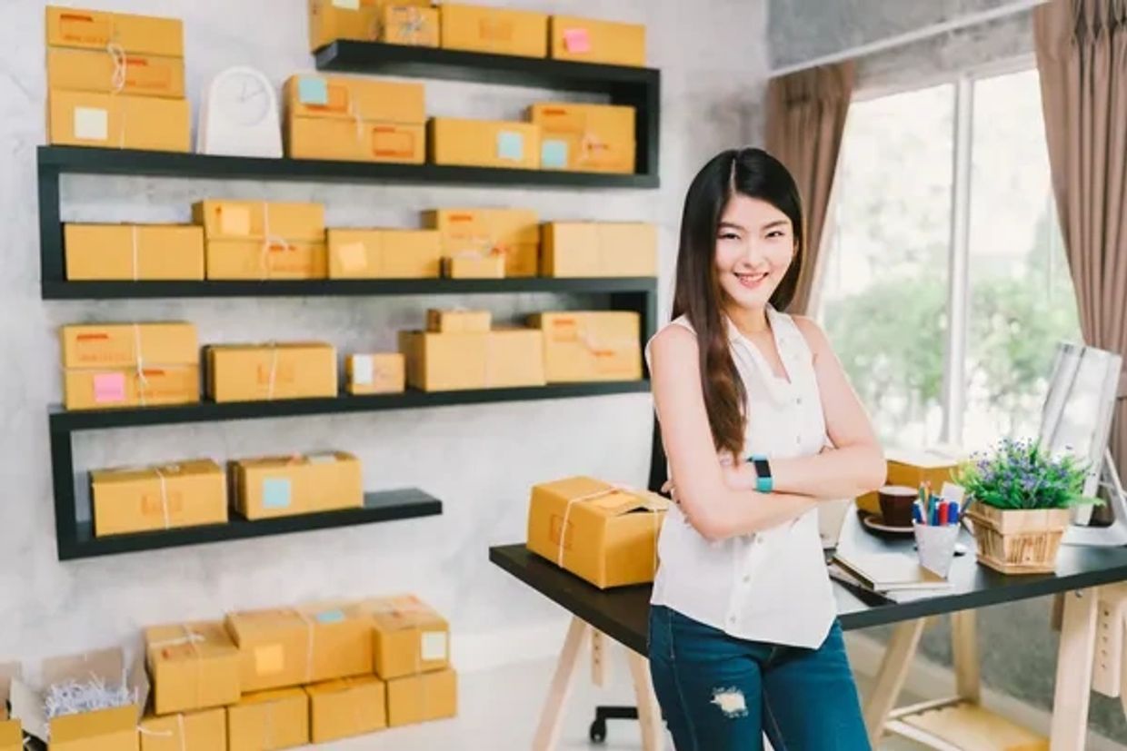 Smiling woman with crossed arms in a room filled with packaged boxes.