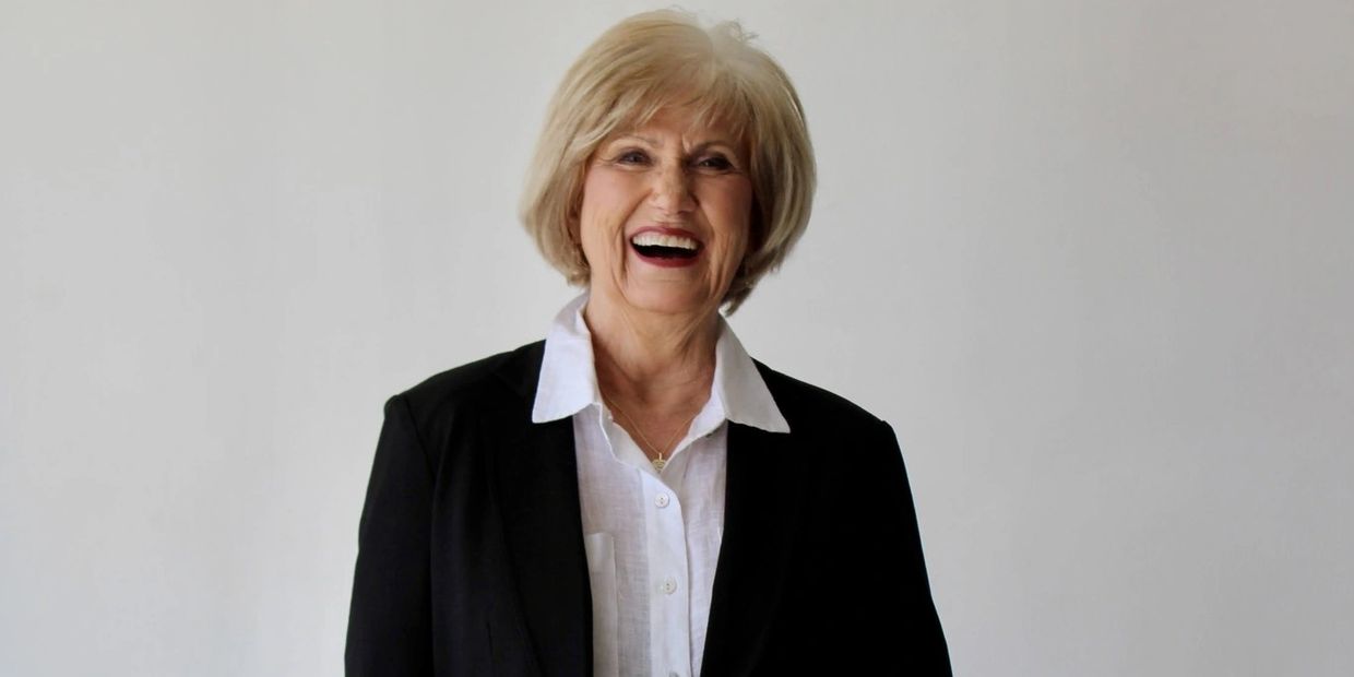 Older woman in a black suit smiling confidently against a white background.