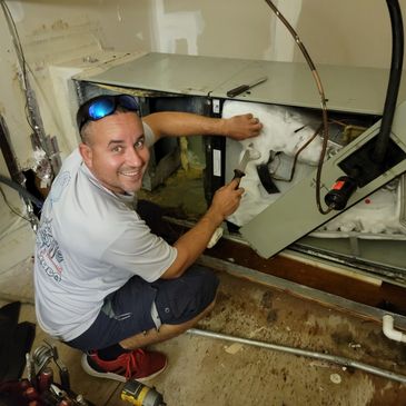 Technician repairing a heavily iced HVAC unit indoors.