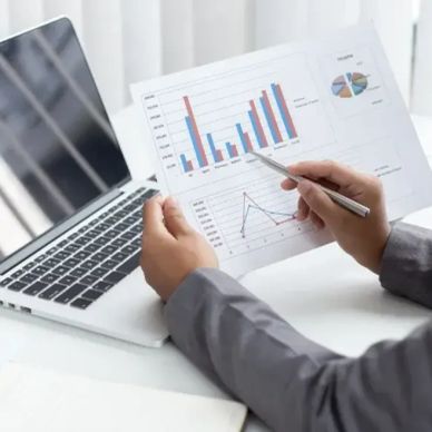 Person analyzing charts and graphs next to a laptop.