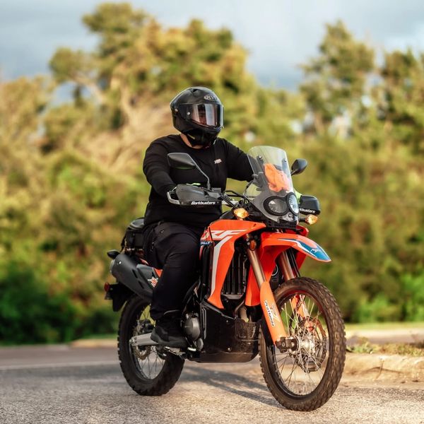 Rider in black gear on an orange adventure motorcycle in a natural setting.