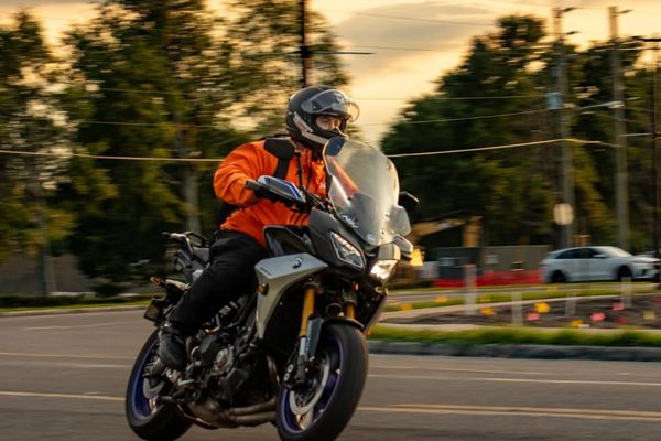 Motorcyclist in orange jacket riding a sport bike at sunset.
