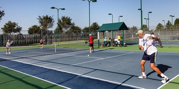 People playing doubles tennis on an outdoor court on a sunny day.