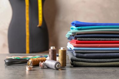 Stack of colorful fabrics with sewing tools on a table.