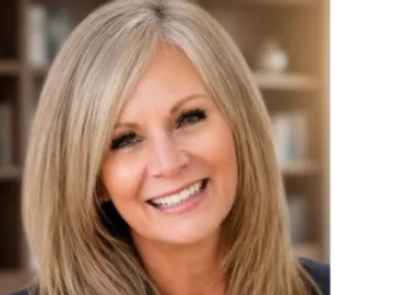 Smiling middle-aged woman with blonde hair in a cozy indoor setting.
