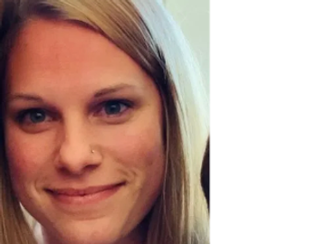 Close-up portrait of a smiling woman with blonde hair and a nose piercing.