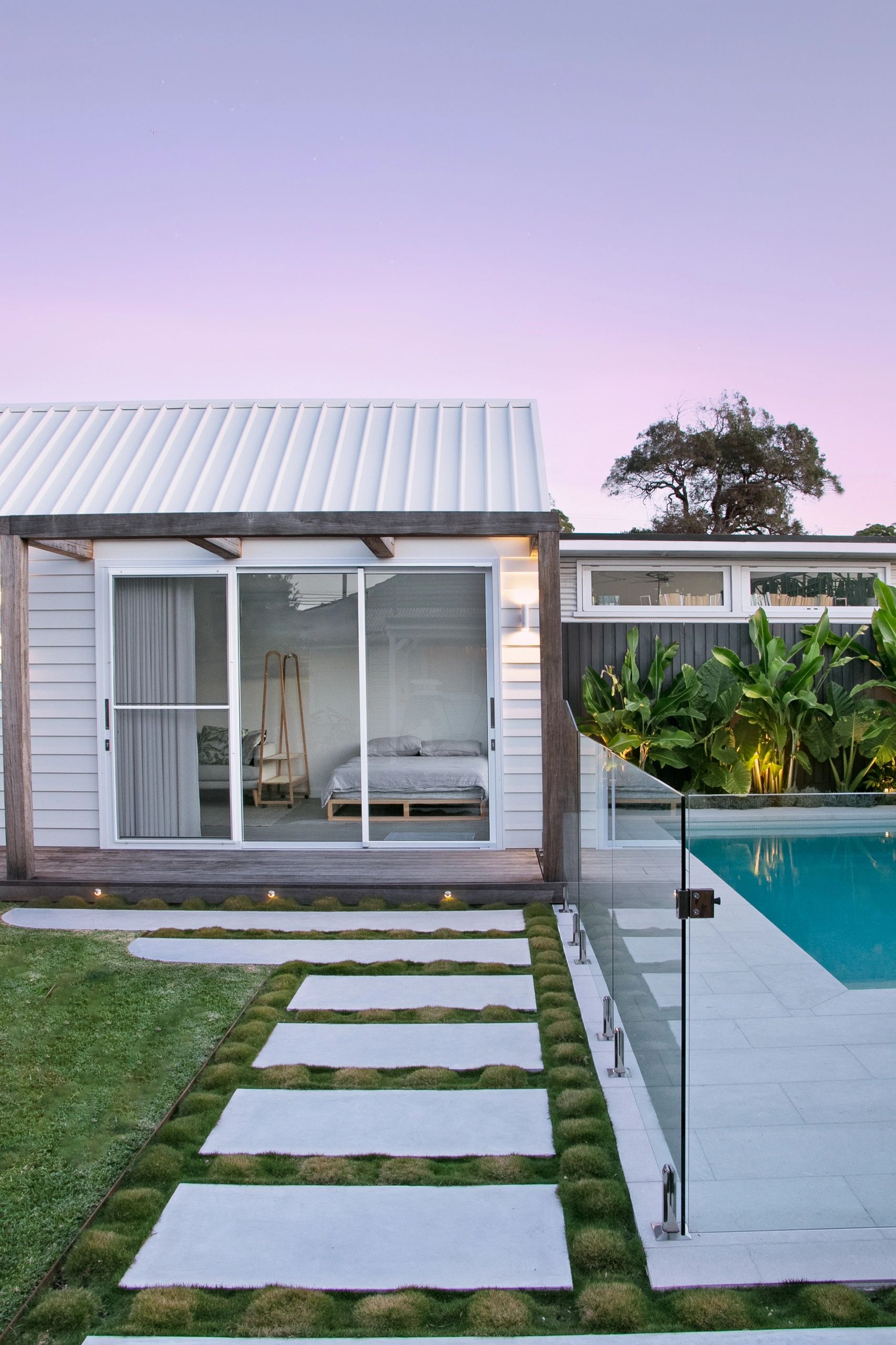 Modern poolside house with glass fence and stepping stones.