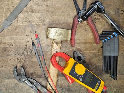 A collection of hand tools including a hammer, pliers, multimeter, and hex keys on a wooden surface.