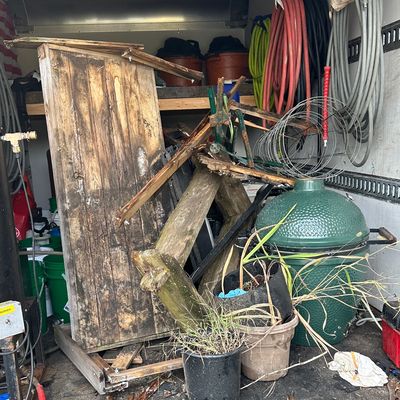 A cluttered storage space with a broken wooden structure, plants, and various tools.