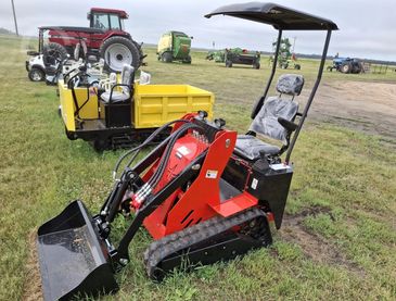 Compact red mini loader with tracks on grass.