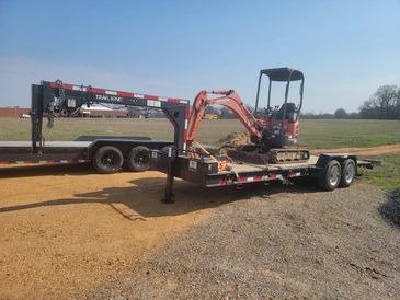 Mini excavator on a flatbed trailer in a rural area.