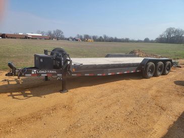 Flatbed trailer with three axles on a dirt road.