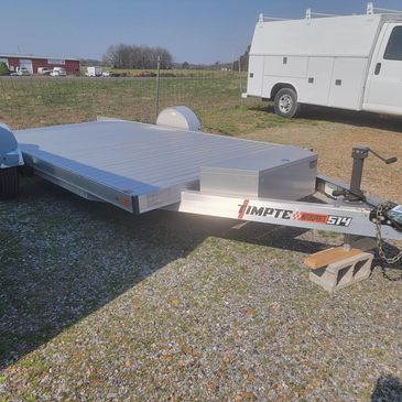 Flatbed trailer parked on gravel with a white service van nearby.