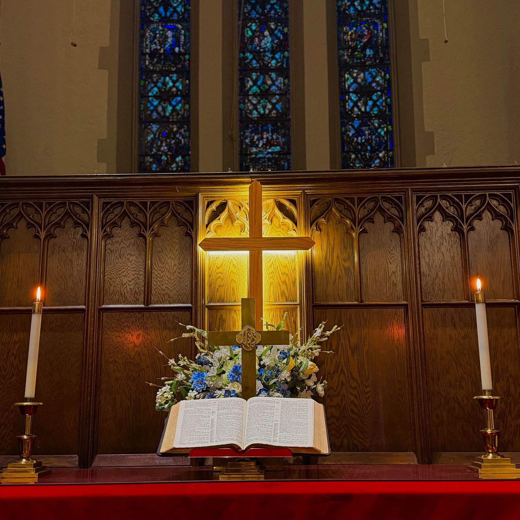Illuminated cross with candles and an open Bible in a church altar.