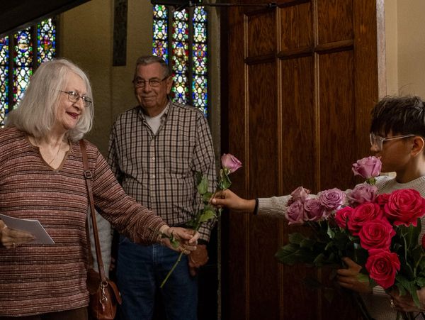 A young person hands a rose to an elderly woman in a church setting.