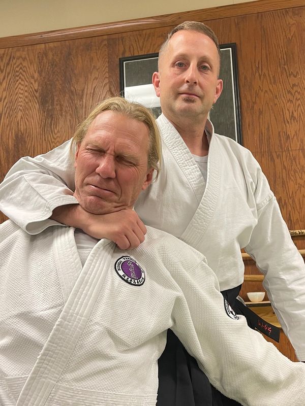 Two men in martial arts uniforms practicing a chokehold.