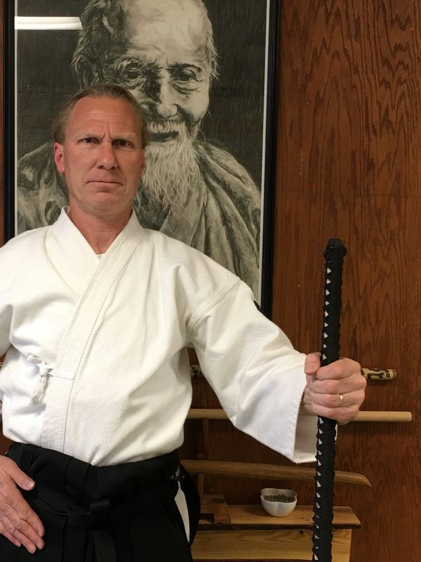 A martial artist with a sword in front of a portrait of an elderly man.