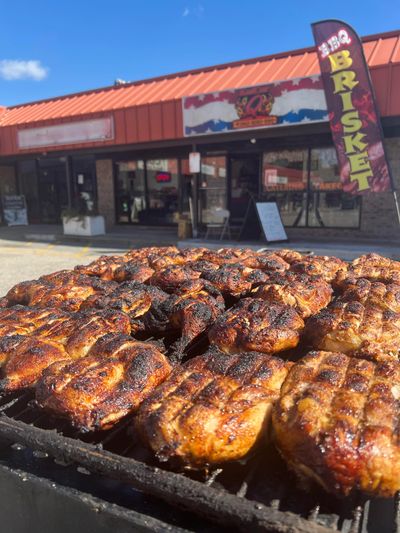 Grilled chicken pieces cooking on an outdoor BBQ grill in front of a BBQ restaurant.