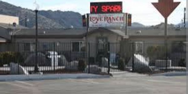 View of a parking lot and building with a fence and a sign above the entrance.