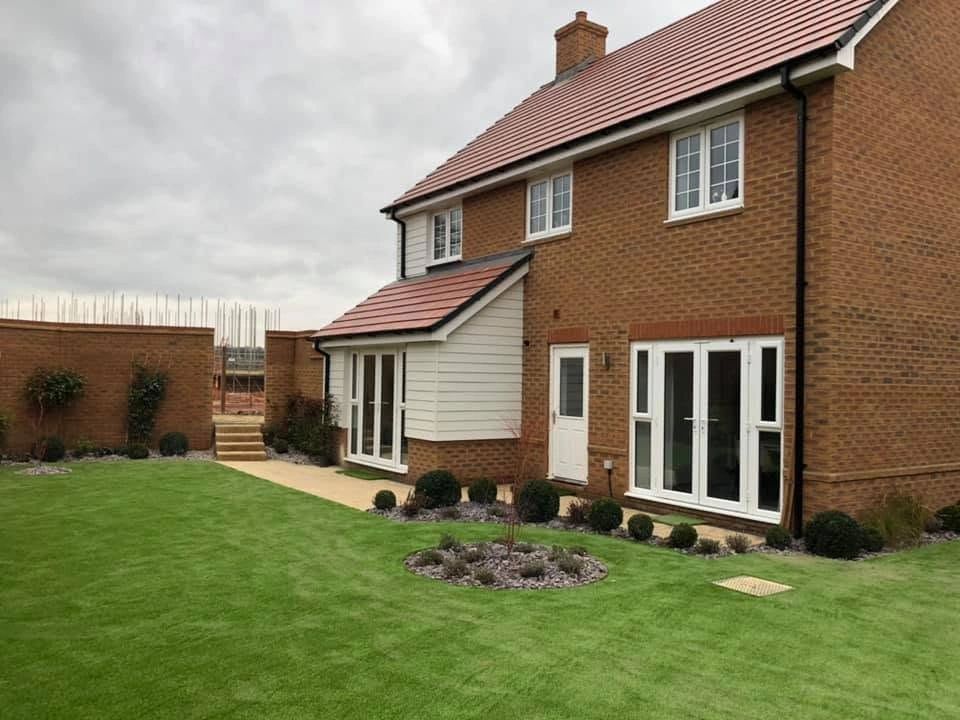 Modern brick house with a neatly landscaped backyard and cloudy sky.