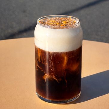 Foamy cold brew coffee with cream in a clear glass on a tan table.