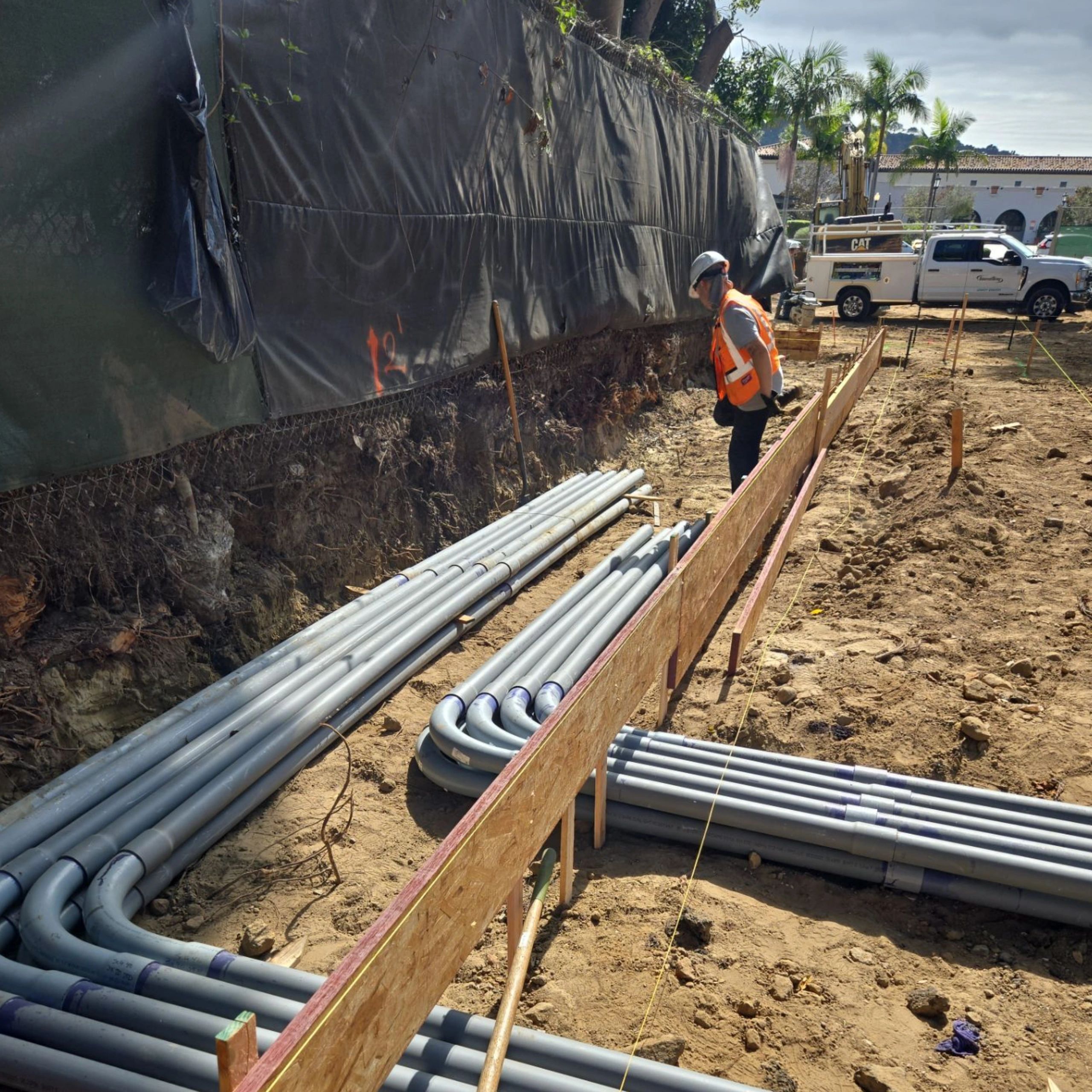 Construction worker inspects electrical conduit installation at a building site.