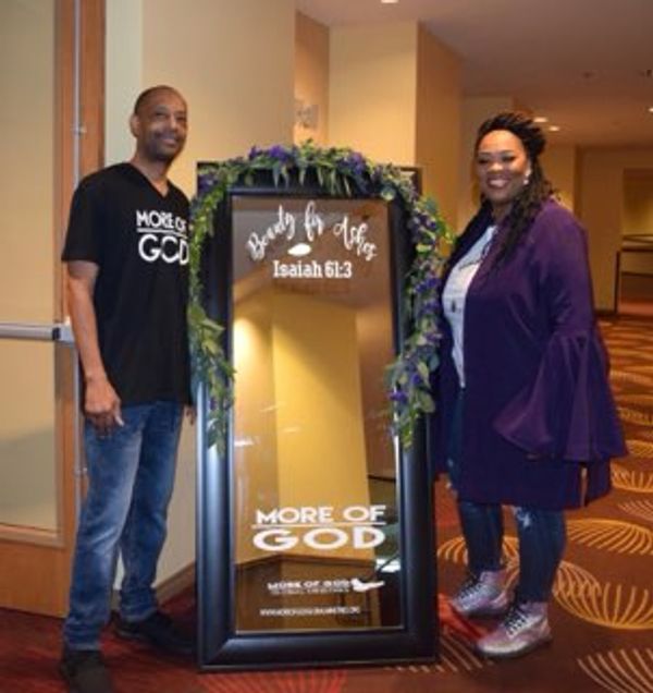 Two people posing with a decorated mirror displaying a religious message.