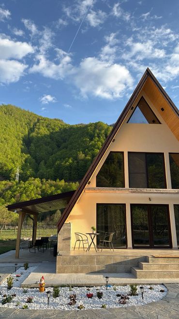 A-frame house with outdoor seating surrounded by green hills under a blue sky.