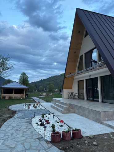 A modern A-frame house with a landscaped garden and cloudy sky.