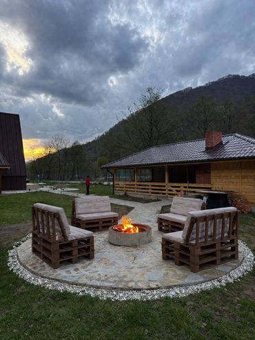 Outdoor fire pit surrounded by wooden pallet chairs at dusk.