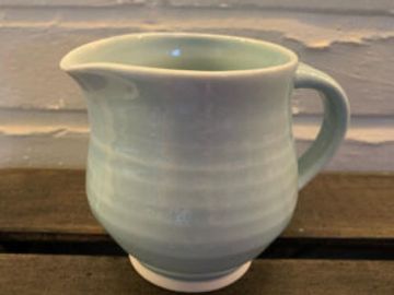A pale green ceramic pitcher with a handle and spout on a wooden surface.