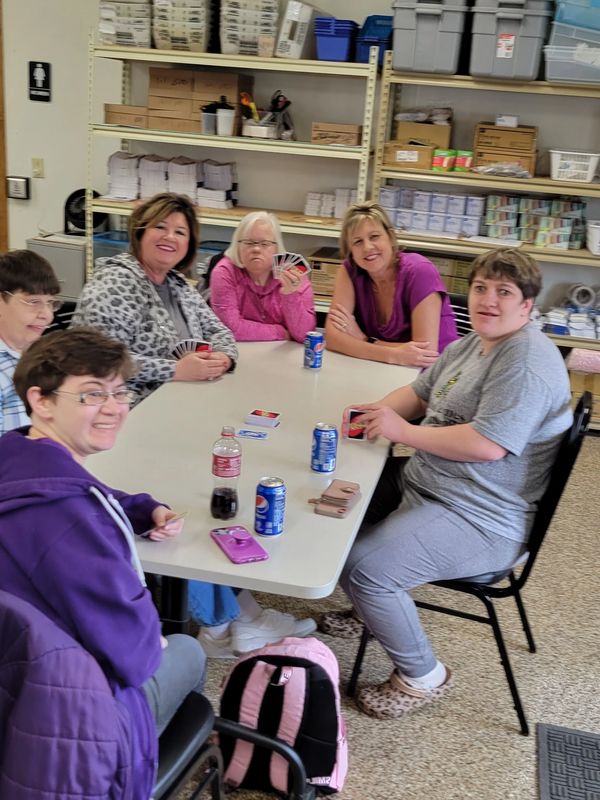 Group of six people playing cards around a table in a cozy room.