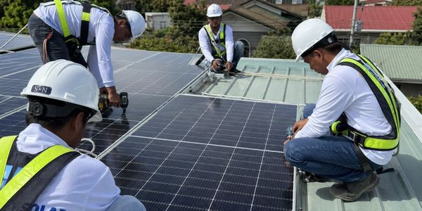 Workers installing solar panels on a rooftop with safety gear.