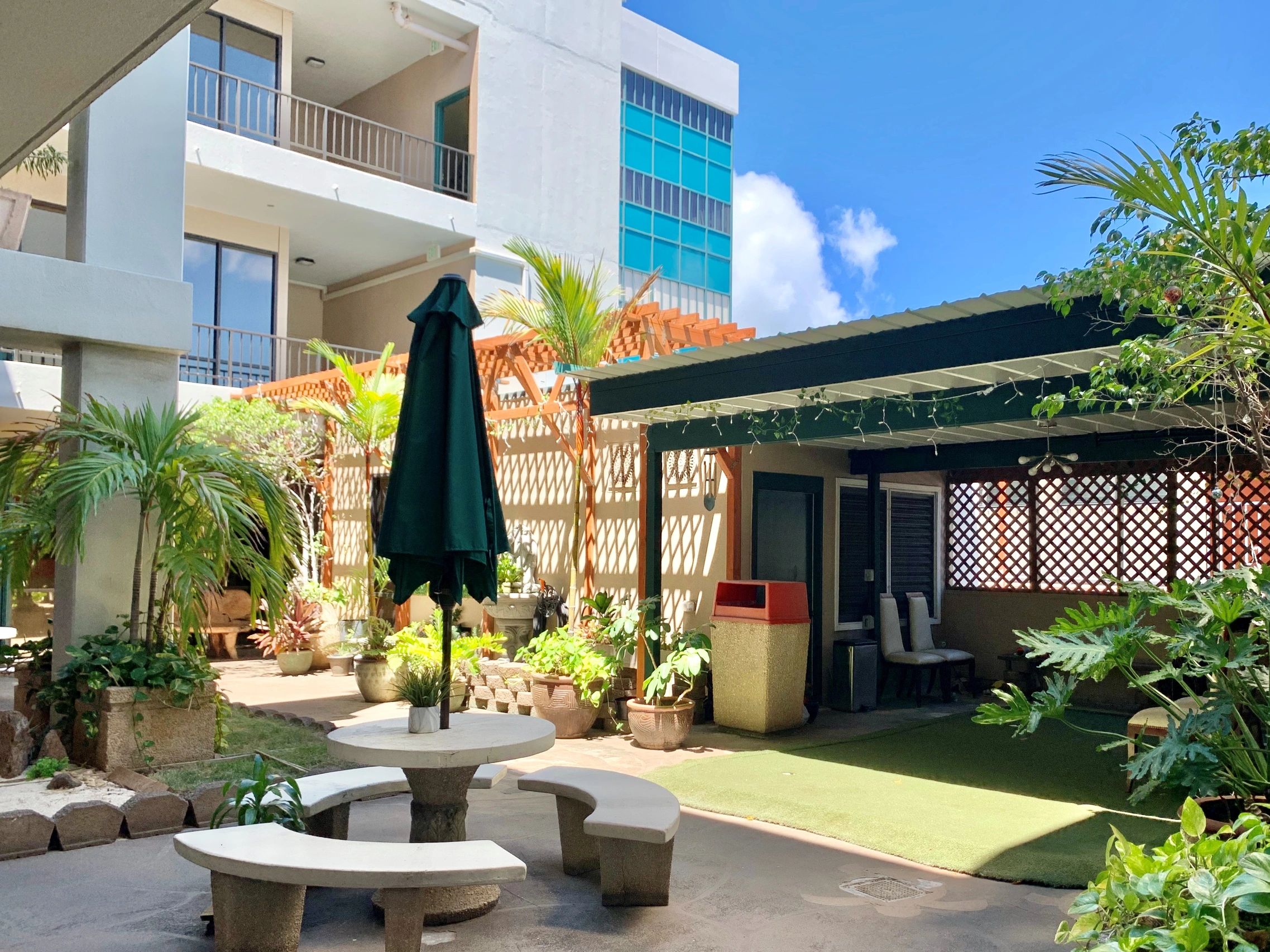 Outdoor patio with greenery and seating area under blue sky.