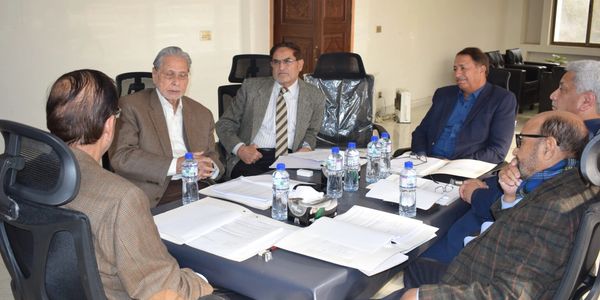 A group of men in suits having a formal meeting around a table with documents and water bottles.