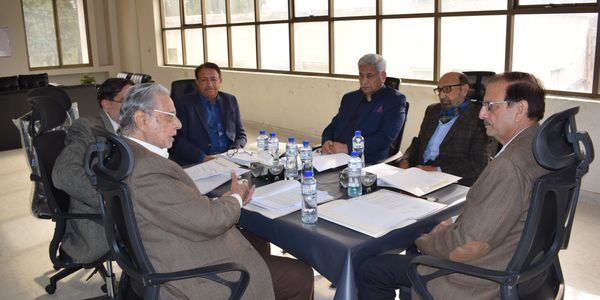 Six men in suits having a formal meeting around a table with documents and water bottles.