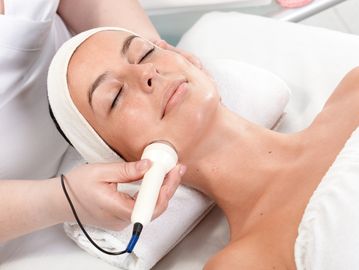Woman receiving microneedling on the neck and chest using a safe, handheld skin-rejuvenating device.