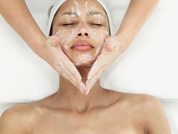 Woman receiving a spa facial with hands gently placed on her chest and neck, showing décolleté care.