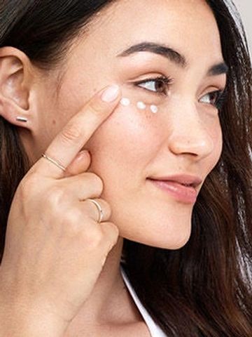 Woman touching under-eye area with finger, demonstrating skincare focus on puffiness and fine lines