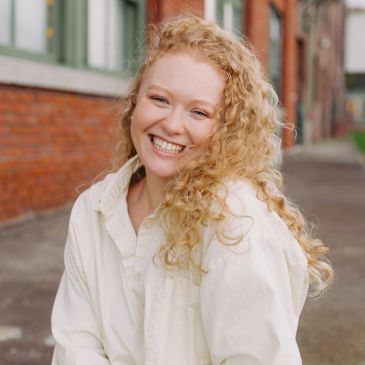 Smiling woman with curly hair outdoors.