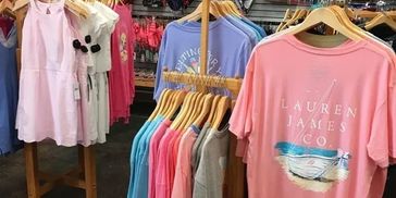 Colorful dresses and t-shirts on wooden hangers in a store.