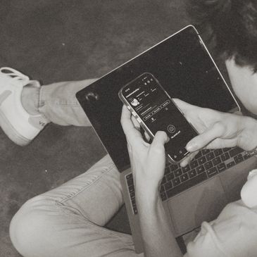 Person sitting cross-legged using a smartphone and laptop.