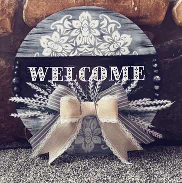 Round wooden welcome sign with floral design and a bow.