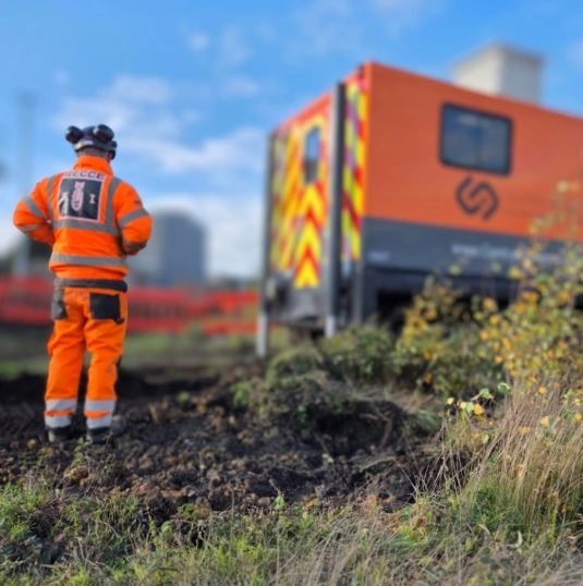 Worker in orange safety gear at a construction site near an orange vehicle.