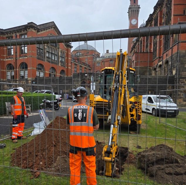 Construction workers with excavator digging in front of historic buildings.