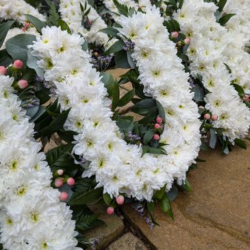 White funeral flower tribute with chrysanthemums and pink berries arranged in lettering